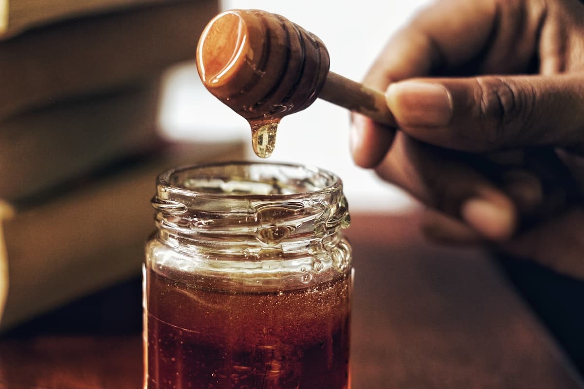 Glass jar of golden honey beside a piece of honeycomb in warm natural light